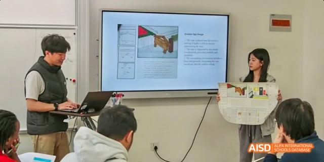 A teacher from JPED Academy, presenting on a large screen to a class.