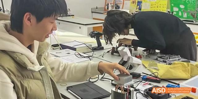 A student from JPED Academy, using a computer and a piece of equipment for a project.