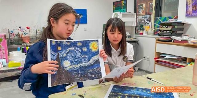 Two female students from JPED Academy, sitting together and looking at a book about Vincent van Gogh's "The Starry Night."