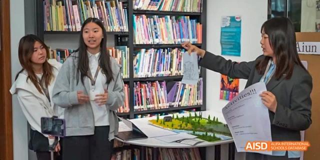A female student from JPED Academy, standing in a library with books on the shelves.