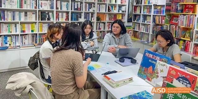 A group of students from JPED Academy, sitting at a table in a library with books and papers.