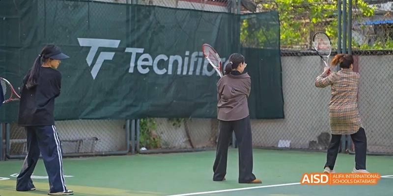 A student from JPED Academy, playing tennis on a court with a "Tecnifibre" banner in the background.
