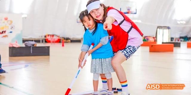 A young student from JPED Academy, learning to play floorball with a girl leaning on her back.