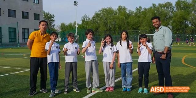 A group of students from JPED Academy, in white t-shirts, standing in a line on a sports field with a teacher.