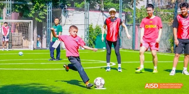 A student from JPED Academy, kicking a soccer ball on a green field during a game.