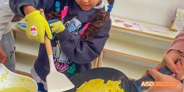 A young student from JPED Academy, cooking eggs with a spatula during a class activity.