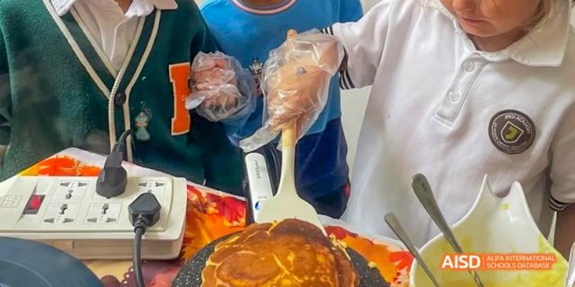 A person from JPED Academy, wearing plastic gloves and serving food from a pan with a spatula.