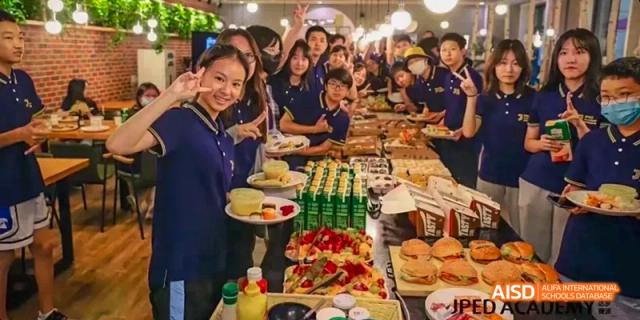 A group of students and teachers from JPED Academy, posing with food at a buffet table during an event.