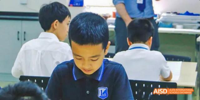 A male student in a school uniform looking down at his desk, Léman International School Chengdu