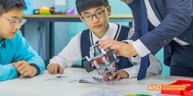 A male student holding and examining a small robot he built, Léman International School Chengdu