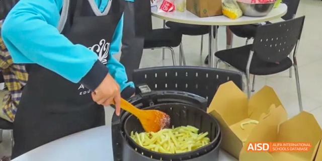 A person stirring food in a large pan at a food stall, Léman International School Chengdu