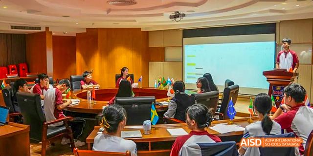 A teacher leading a presentation from the front of a classroom with students seated at tables at Majestic International College.