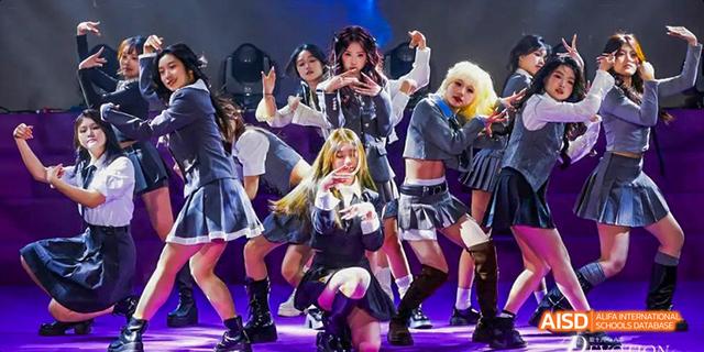 A K-pop style dance group performing on stage with bright lights at a Majestic International College event.