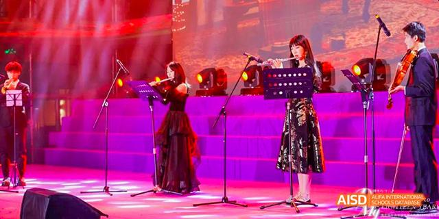 A musician playing a violin on stage with other performers in the background at an event for Majestic International College.