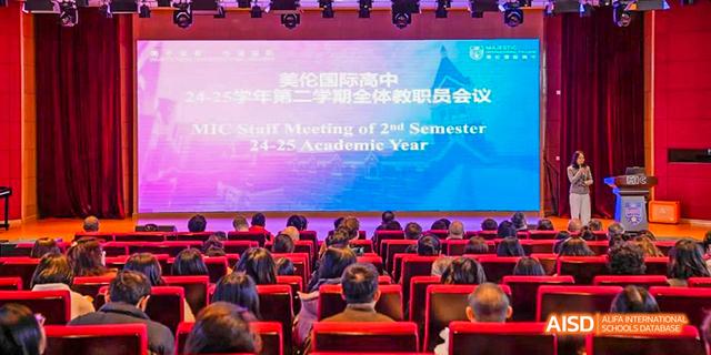 An audience of people seated in an auditorium, with a large screen displaying "Staff Meeting of 2nd Semester 24-25 Academic Year" and the name Majestic International College.