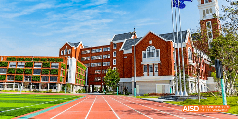 An outdoor view of a red brick school building with a running track and green field at Majestic International College.