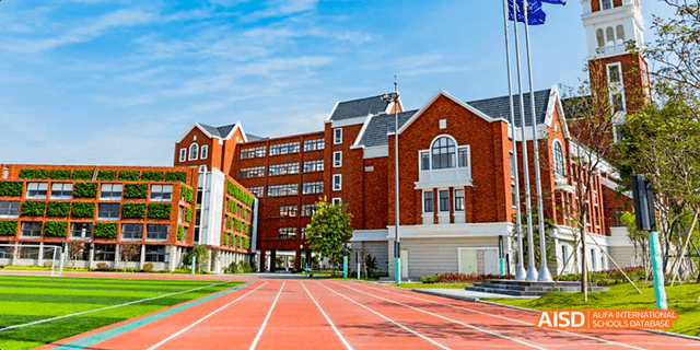 An outdoor view of a red brick school building with a running track and green field at Majestic International College.