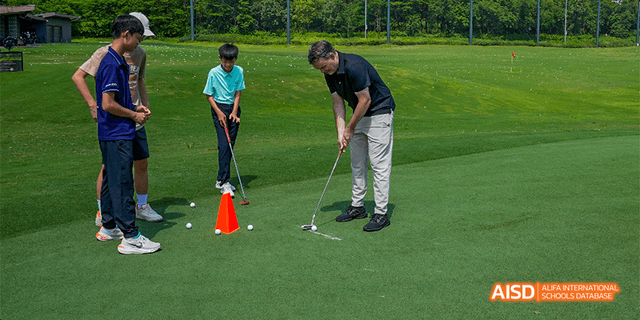 Two students practicing their golf putting skills with a small cone marker on a green field at Majestic International College.