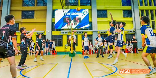 Students on a basketball court during a game, with a large screen displaying a logo in the background at Majestic International College.