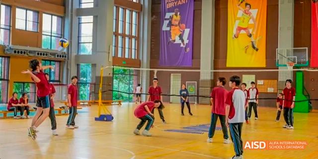Students playing an indoor volleyball game in a school gym with a large banner hanging in the background at Majestic International College.