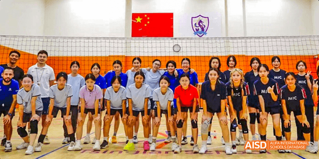 A group of students smiling and posing together in a line, with the Chinese national flag and a school flag behind them at Majestic International College.