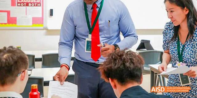 A teacher in a red tie is talking to two students in a classroom at Malvern College Chengdu.