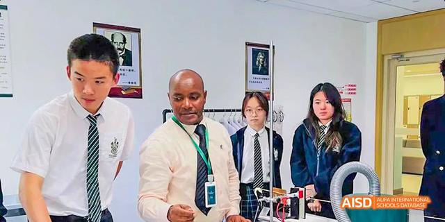 An adult in a white shirt and lanyard is posing with two students at Malvern College Chengdu.
