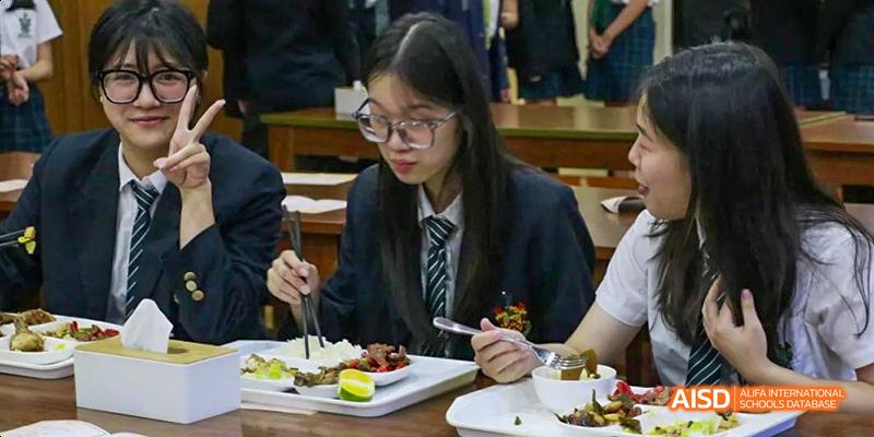 A female student in a school uniform with a tie and glasses is eating a meal at a table at Malvern College Chengdu.