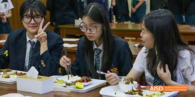 A female student in a school uniform with a tie and glasses is eating a meal at a table at Malvern College Chengdu.