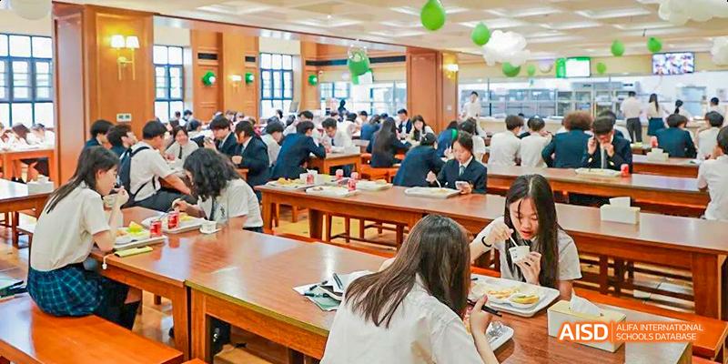 A wide shot of the school cafeteria, showing students in uniforms eating at long tables at Malvern College Chengdu.