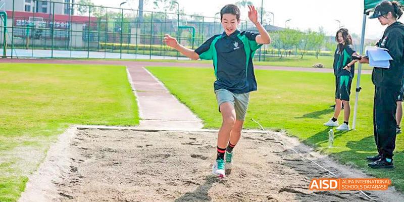 A student is running on a red track with his arms raised, celebrating at Malvern College Chengdu.