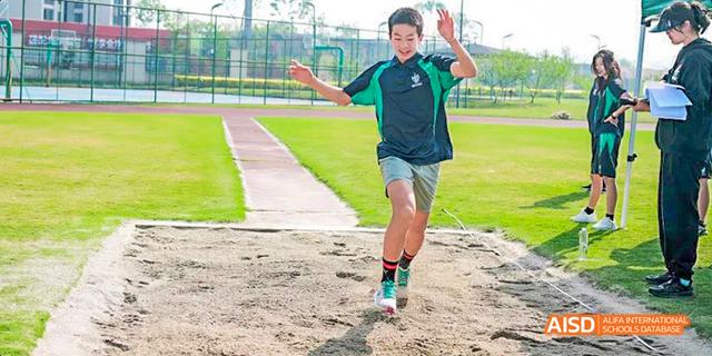 A student is running on a red track with his arms raised, celebrating at Malvern College Chengdu.