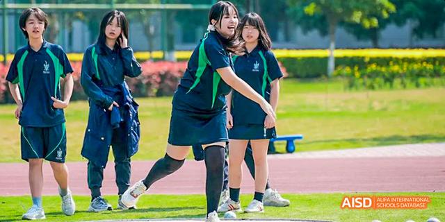 Two female students are walking together on a green field, looking down at Malvern College Chengdu.