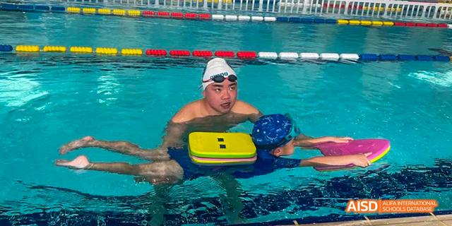 A student wearing a swim cap, goggles, and a kickboard is in a swimming pool at Malvern College Chengdu.