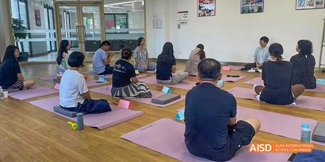 A group of people are sitting on yoga mats, meditating in a room at Malvern College Chengdu.