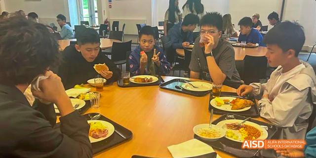 Students are sitting at a table in the cafeteria, eating meals and looking at their phones at Malvern College Chengdu.