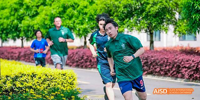 Two male students in green and blue shirts are running on a field with trees in the background at Malvern College Chengdu.