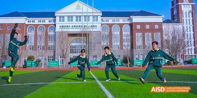 Two students running on a sports field with the school building in the background at Maple Leaf International School - Luoyang.