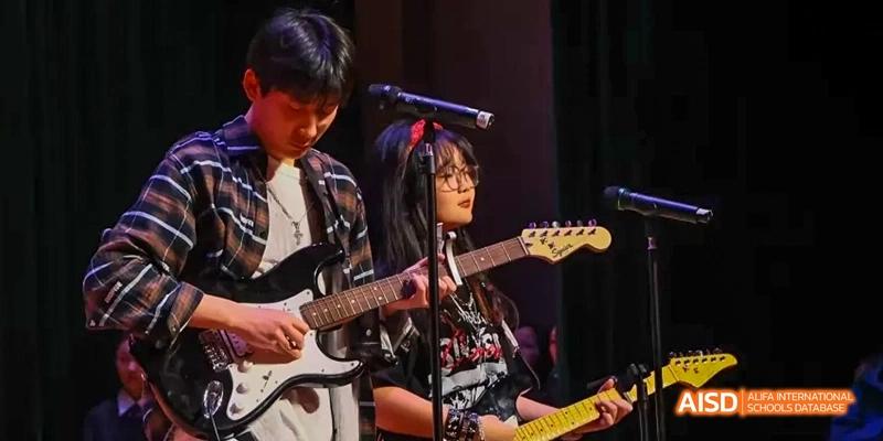 A female student playing an electric guitar on stage at Maple Leaf International School - Luoyang.