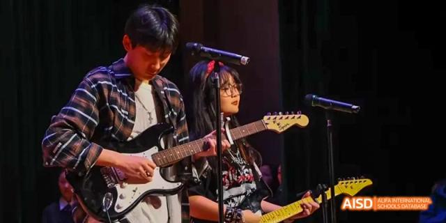 A female student playing an electric guitar on stage at Maple Leaf International School - Luoyang.