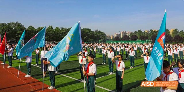 Students in uniform carrying a flag on a sports field at Maple Leaf International School - Luoyang.
