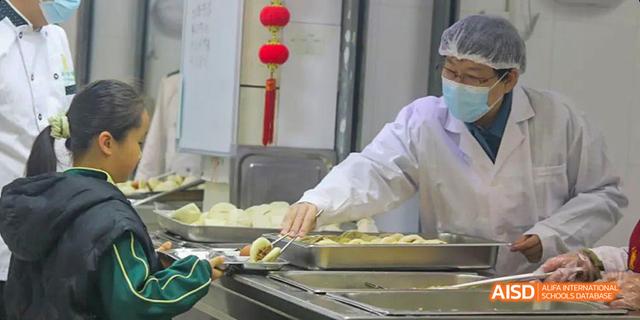 A person in a white jacket preparing food at Maple Leaf International School - Luoyang.