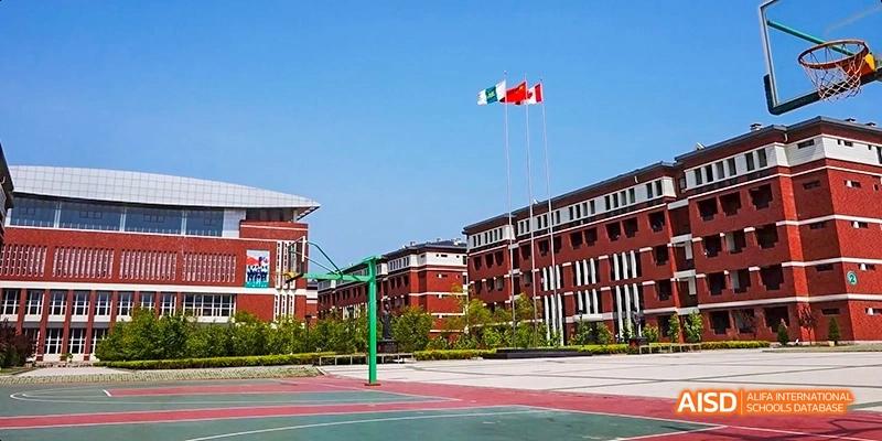 A view of the outdoor basketball court and school buildings with flags at Maple Leaf International High School - Dalian