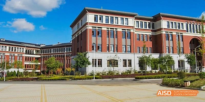 An exterior view of a red brick school building with a manicured lawn at Maple Leaf International High School - Dalian