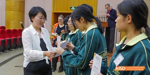 A group of female students from Maple Leaf International High School - Dalian, one of whom is receiving a certificate from a teacher.