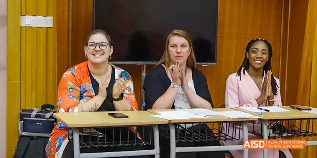 A female student and two teachers from Maple Leaf International High School - Dalian are clapping and sitting at a desk.