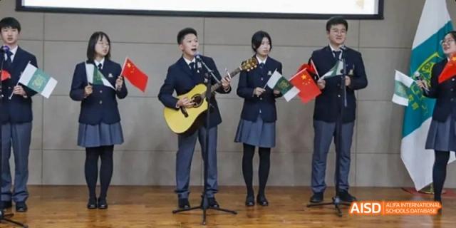 A male student from Maple Leaf International High School - Dalian playing the guitar, and a female student singing on stage.