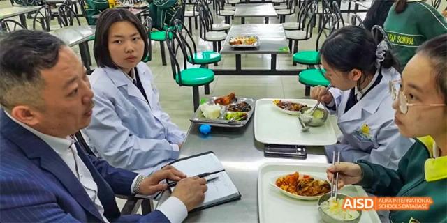A student from Maple Leaf International High School - Dalian is sitting at a table with food in a cafeteria.