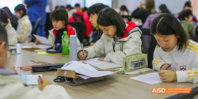 A student from Beijing Aidi School wearing a white and red jacket, studying at a desk.
