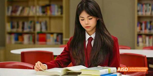 A portrait of a female student from Beijing Aidi School in a red uniform, sitting and reading in a library.